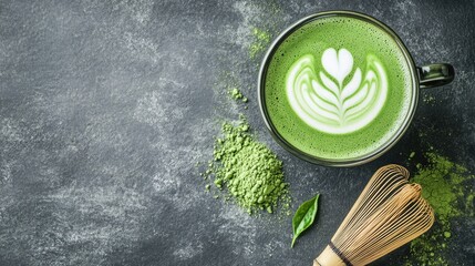 A matcha latte with foam art, placed on a slate surface, with matcha powder sprinkled around and a matcha whisk artistically leaning against the cup.