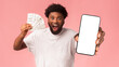 © Prostock-studio - Making good money by phone. Happy african man showing blank smartphone screen and bunch of money, pink background