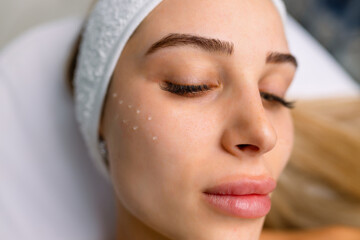 Wall Mural - Beautiful relaxed woman at beautician cabinet receiving anti wrinkle injections on cheekbones, lying with closed eyes in beauty salon