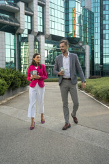 Wall Mural - Confident business people in a discussion while walking with coffee. Mature professionals having a discussion at coffee break in front og glass building exterior.