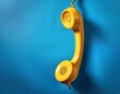 © MRSUTIN - A bright yellow telephone receiver hangs against a vibrant blue background.  (1)