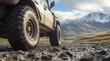© Creative Art7 - Close-up of off-road tires on an overland vehicle, with rugged terrain in the background