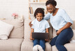 © Prostock-studio - Distance Education Concept. African mother helping her child with homework, using laptop, sitting on sofa at home. Free space