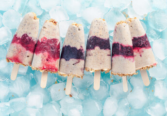 Wall Mural - Homemade ice cream popsicle with berries, granola and chia seeds. Healthy summer breakfast concept. Popsicles from yogurt and banana with berries and granola. Top view. Copyspace