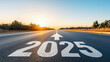 © Maksym - A long, straight road stretches into the horizon at dawn, with '2025' painted in bold white letters on the asphalt, a large arrow pointing forward, and the sunrise casting a golden