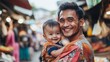 © Leli - A young dad beams with happiness while holding his smiling toddler in a bustling market