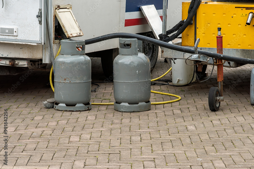 two gray steel gas bottles stand outside on the street next to a market stall