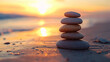 © Sawyer0 - Na tle pięknego zachodu słońca, na plaży, z równowagą ustawiony stos kamieni zen symbolizuje harmonię i wewnętrzny spokój.