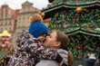 © Maryia - Mother lovingly hugs her son in front of a beautifully decorated Christmas tree at a festive European Christmas fair. Concept for Christmas holidays and family holidays. High quality photo