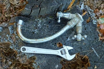 one small new iron adjustable industrial mechanical shiny chrome wrench lies with dirty plumbing broken old faucet lie  on wooden stump day outdoors