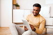 © Prostock-studio - Afro Man Using Digital Tablet Reading Book Online Sitting On Floor At Home. Selective Focus