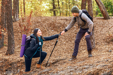 Handsome man hiker helping his girlfriend uphill in forest, couple hiking together