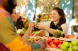 © DC Studio - Friendly farmer offering samples to customers, showcasing homegrown fruits and vegetables at local farmers market. Young multiracial couple or family tasting natural fresh produce, visiting food fair.