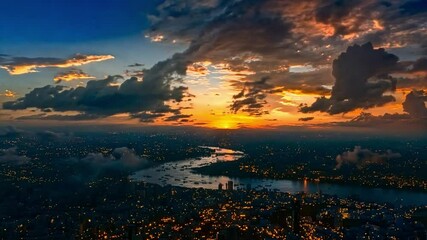 Poster - The sun sets behind the city, casting golden hues across the skyline while clouds enhance the vibrant colors over the peaceful river below.