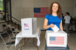 © Alan - portrait of a smiling woman voting in the us election, placing vote ballot in the polling box, vote in America. Concept of choice, democracy and freedom