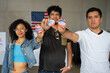 © Alan - group of Hispanic people holding 2024 Vote election I voted buttons or pins at a US election polling station. In the background, american flag at the background, concept of latin or latino vote
