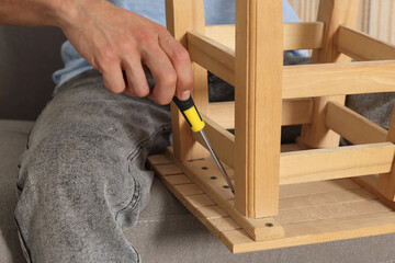 Canvas Print - Man repairing wooden stool with screwdriver indoors, closeup