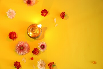 Wall Mural - Diwali celebration. Diya lamp and beautiful flowers on yellow background, flat lay. Space for text