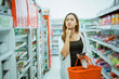 © Odua Images - young woman thinking about what to buy while shopping carrying a cart at a minimarket