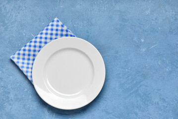 Empty plate and checkered napkin on blue table