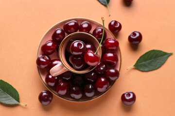 Cup and plate with sweet cherries on orange background