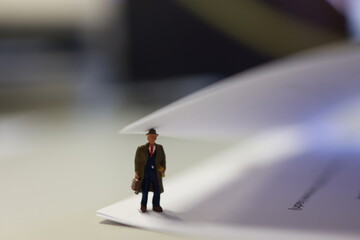 Micro person, business male with suitcase, standing under the page of paper in the office.