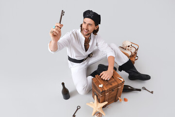 Young pirate with chest and key on light background