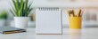 © MNFTs - A clean, blank notepad sits on a modern desk alongside plants and stationery, perfect for inspiration and productivity.