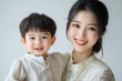 © Yuki Liu - Young Chinese mother and cute son interacting and smiling in front of a plain background, dressed in simple clothes, during a family photo portrait shoot.
