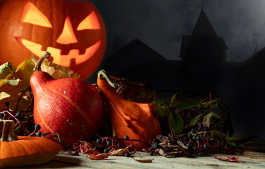 Halloween pumpkin head Jack lantern with dried-up leaves on a background of old house.