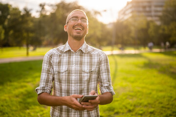 Portrait of cheerful adult man in park who is using smartphone.