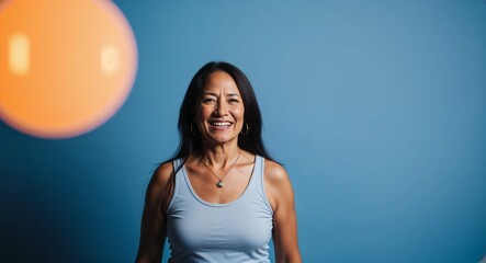 Happy middleaged Hispanic woman with long hair wearing tank top on plain blue background