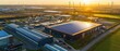© TPS Studio - Aerial view of an industrial area with solar panels, wind turbines, and a sunset, showcasing renewable energy and modern infrastructure.