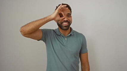 Canvas Print - Young hispanic man standing with ok sign on hand, smiling and looking through fingers with happy expression over isolated white background