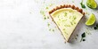 © Kamonwan - Delicious key lime pie slice with a crumb crust, garnished with lime zest and fresh lime wedges on a marble background.