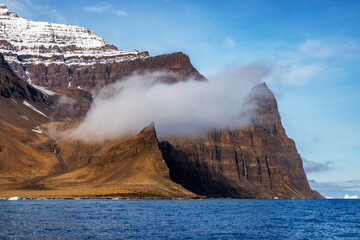 Wall Mural - low cloud hangs in the red rock mountains of scoresby sund, eastern greenland. this fjord system is 