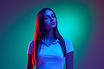 Young attractive girl dressed casual attire gazes at camera confidently against gradient studio background in mixed neon light. Concept of human emotions, business, beauty and fashion, sales season.