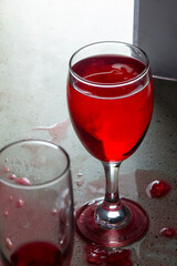 A glass of red liquid was placed next to a glass of wine that was empty and spilled on the granite table with a terrazzo texture