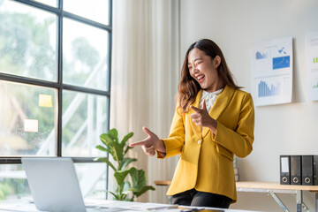 Wall Mural - excited asian businesswoman pointing both index fingers during video call in office