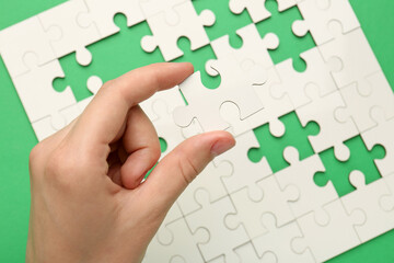 Wall Mural - Woman solving white puzzle on green background, closeup