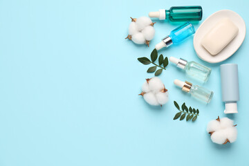 Poster - Different cosmetic products, leaves and cotton flowers on light blue background, flat lay. Space for text