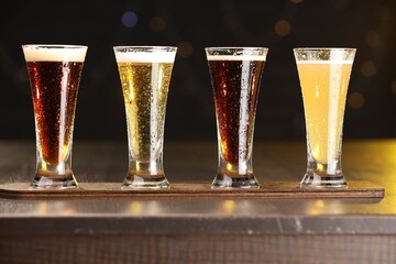 Poster - Glasses with different types of beer on wooden table against blurred lights, closeup