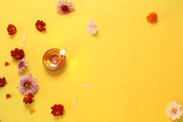 Diwali celebration. Diya lamp and beautiful flowers on yellow background, flat lay. Space for text