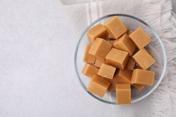 Poster - Tasty sweet caramel candies in bowl on light grey table, top view. Space for text