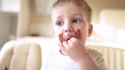 baby boy eat chocolate. dirty little baby kids in the kitchen eating chocolate in the morning. happy family eating sweets kid dream concept. baby dirty face eating lifestyle chocolate cocoa