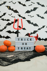 Halloween vertical banner. In the foreground is a sign saying Trick or Treat with devil horns hanging on it and a trident standing next to it. In the background is a decoration with bats. 