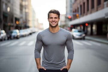 Canvas Print - Portrait of a grinning man in his 20s showing off a lightweight base layer on bustling city street background