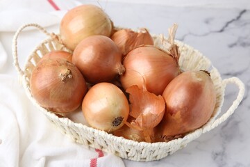 Canvas Print - Fresh onions with peels in wicker basket on light marble table, closeup