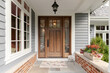© Joseph Hendrickson - A front door and covered porch detail on a home with grey siding, white trim, red brick, a wooden front door.