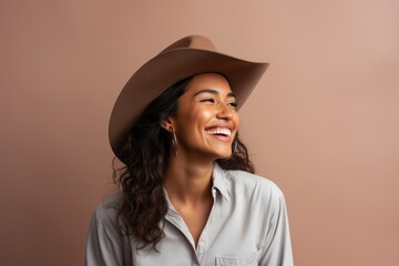 Poster - Portrait of a joyful indian woman in her 20s wearing a rugged cowboy hat over minimalist or empty room background